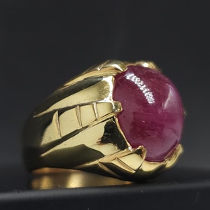 Op de afbeelding: Een gouden ring met een grote, ronde, cabochon geslepen robijn. De ring heeft een gedetailleerde, getextureerde band.
