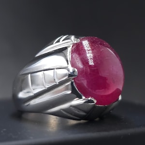 May include: A silver ring featuring a large, round, cabochon-cut ruby gemstone. The ring has a detailed, textured band.