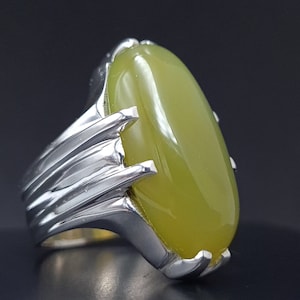 May include: A silver ring with a large, oval-shaped green gemstone. The ring has a detailed, textured band.