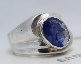 May include: A silver ring with a blue gemstone set in a bezel setting. The ring has a wide band with a textured design.