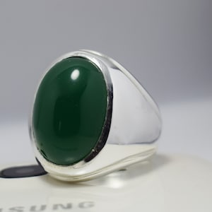 Pode incluir: Um anel de prata com uma grande gema verde oval.