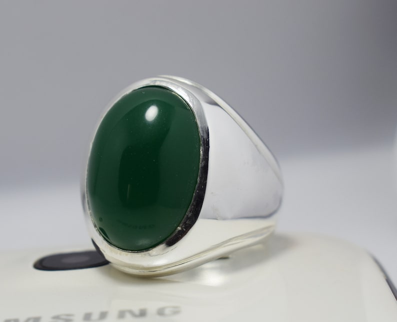 Pode incluir: Um anel de prata com uma grande gema verde oval.