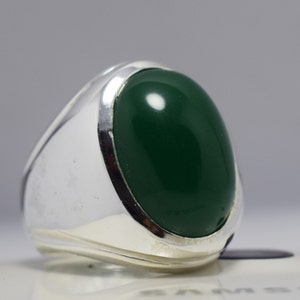 Pode incluir: Um anel de prata com uma pedra oval verde escura.