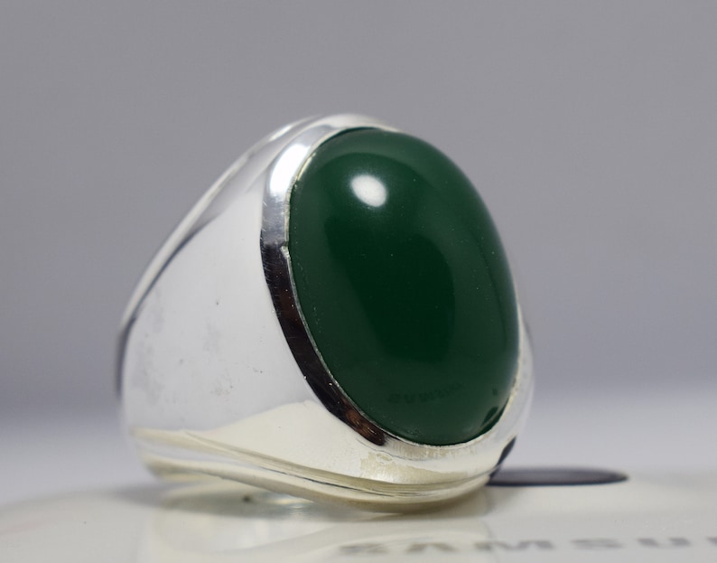 Pode incluir: Um anel de prata com uma pedra oval verde escura.