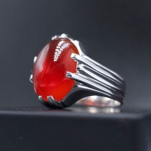 May include: A silver ring with a large, oval-shaped red gemstone. The ring has a detailed, textured band.