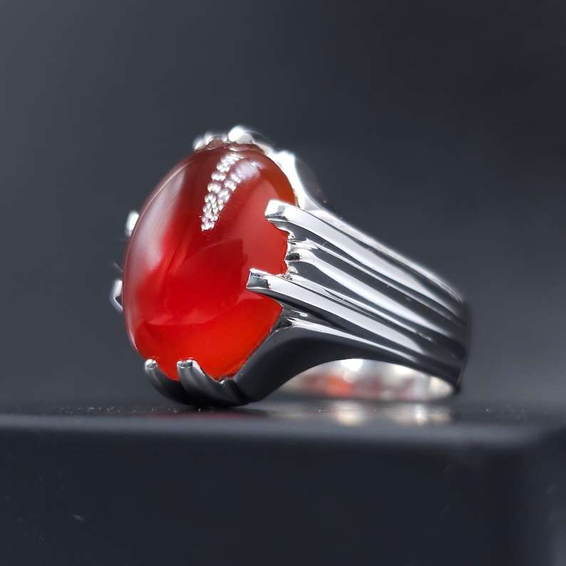 May include: A silver ring with a large, oval-shaped red gemstone. The ring has a detailed, textured band.