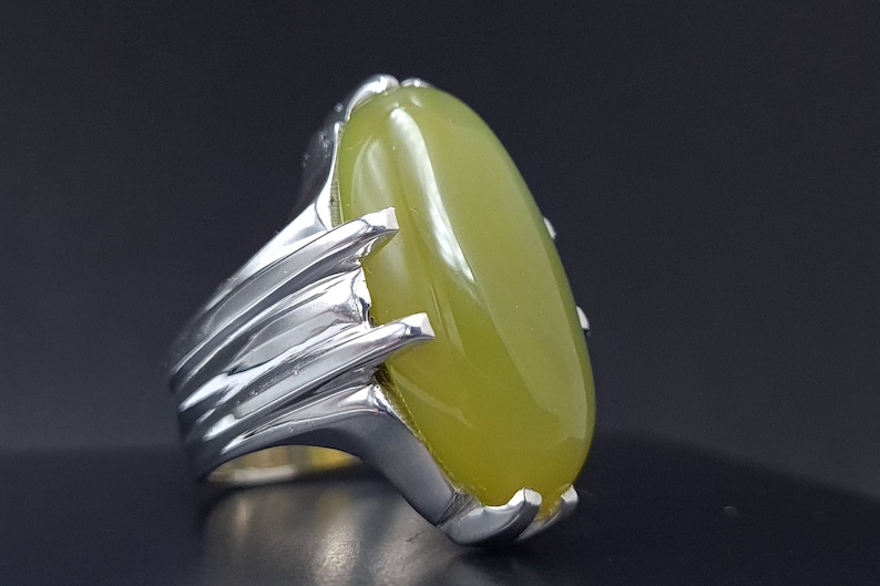 May include: A silver ring with a large, oval-shaped green gemstone. The ring has a detailed, textured band.