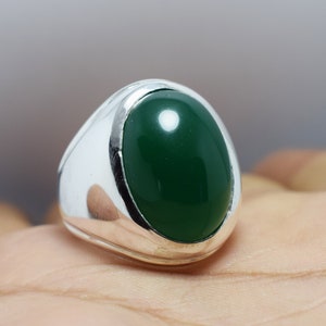 Pode incluir: Um anel de prata com uma grande gema verde oval.