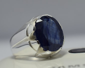May include: A silver ring with a large, oval-shaped blue sapphire gemstone. The ring has a detailed, textured band.