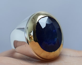 May include: A silver ring with a gold band and a large, oval-shaped blue sapphire gemstone.