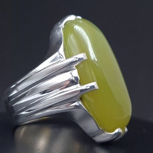 May include: A silver ring with a large, oval-shaped green gemstone. The ring has a detailed, textured band.