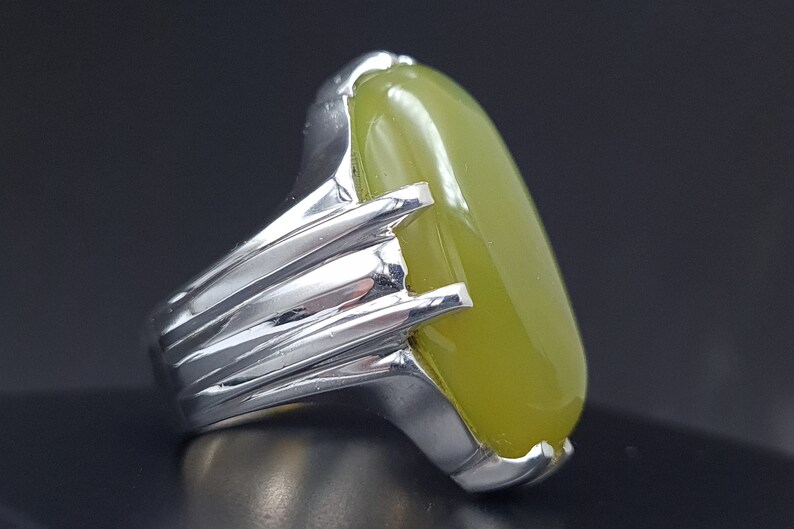 May include: A silver ring with a large, oval-shaped green gemstone. The ring has a detailed, textured band.