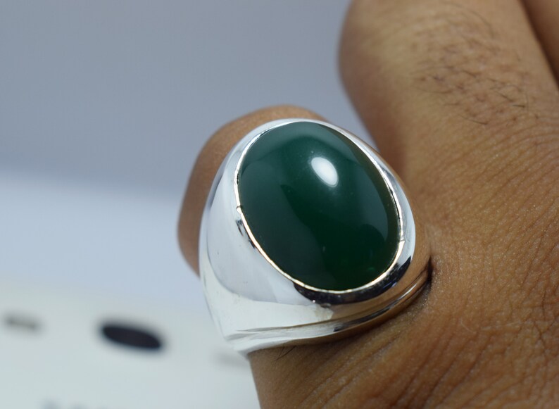 Pode incluir: Um anel de prata com uma grande gema verde oval.