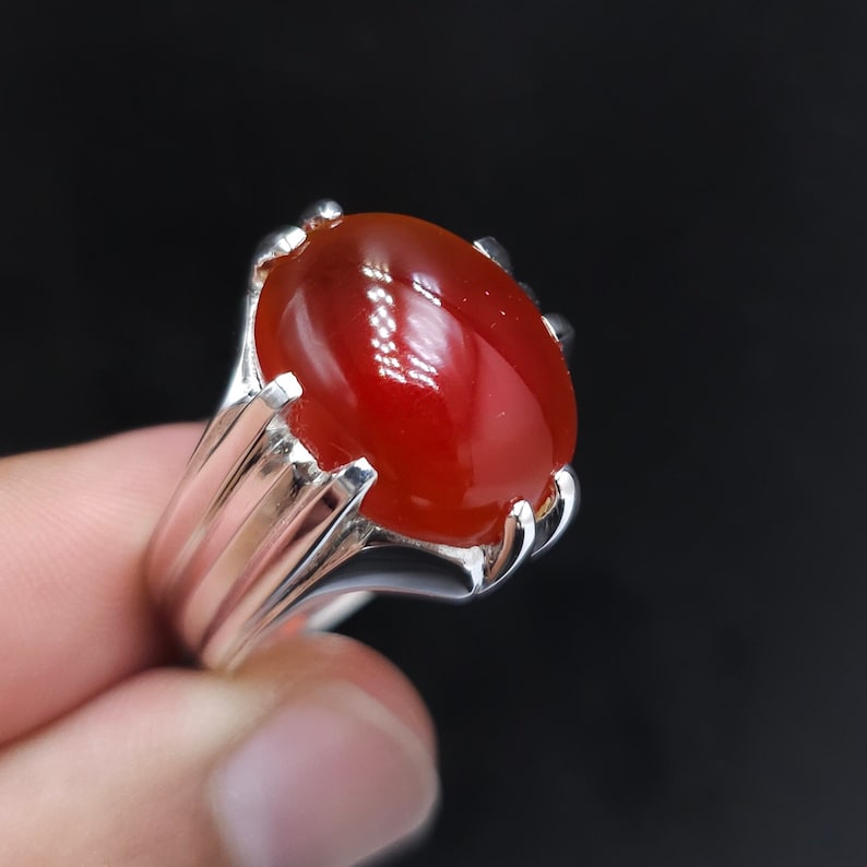 May include: A silver ring with a large, oval-shaped, red gemstone.