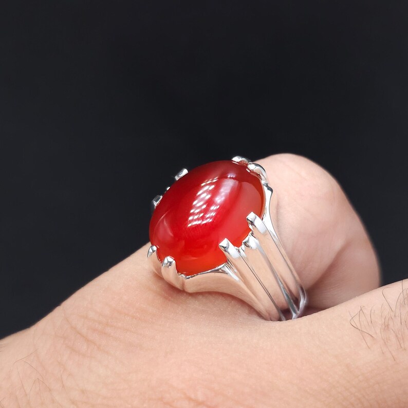 May include: A silver ring with a large, oval-shaped, red gemstone.