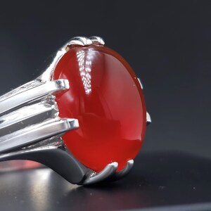 May include: A silver ring with a large, oval-shaped, red gemstone.