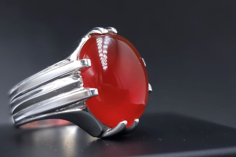 May include: A silver ring with a large, oval-shaped, red gemstone.