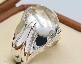 May include: A silver ring with a large, clear, oval-shaped gemstone. The ring has a detailed, textured band.