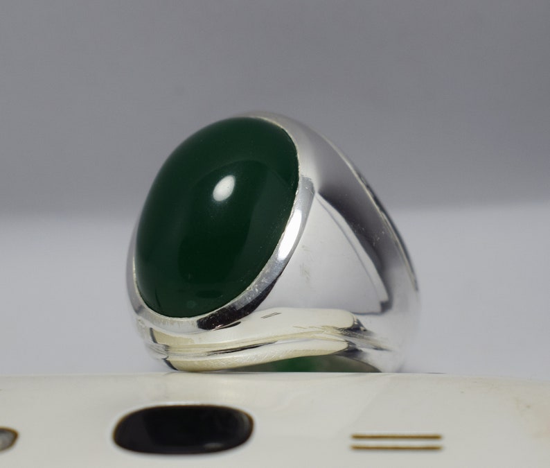 Pode incluir: Um anel de prata com uma grande gema oval de cor verde escura.