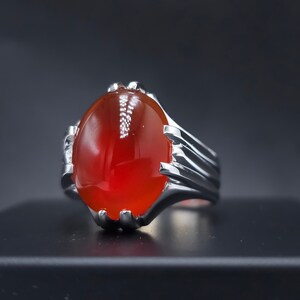 May include: A silver ring with a large, oval-shaped, red gemstone.