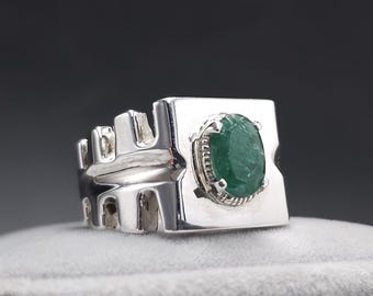 May include: A silver ring with a large, oval-cut green gemstone. The ring has a unique design with a rectangular face and a decorative side. The gemstone is set in a detailed bezel.
