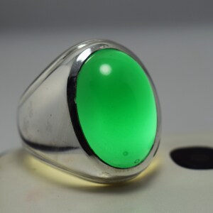Pode incluir: Um anel de prata com uma grande gema verde oval.