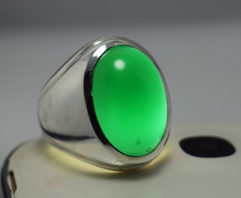Pode incluir: Um anel de prata com uma grande gema verde oval.