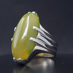 May include: A silver ring with a large, oval-shaped green gemstone. The ring has a detailed, textured band.