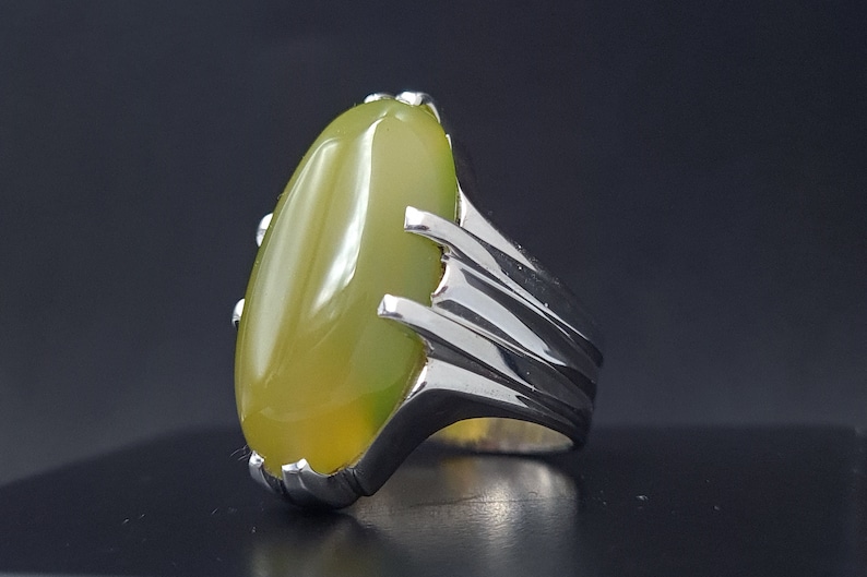 May include: A silver ring with a large, oval-shaped green gemstone. The ring has a detailed, textured band.