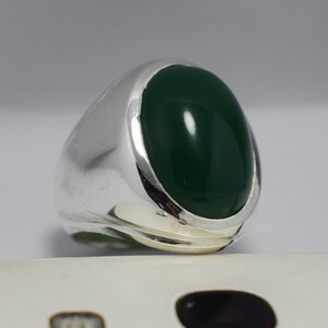Pode incluir: Um anel de prata com uma grande gema verde oval.