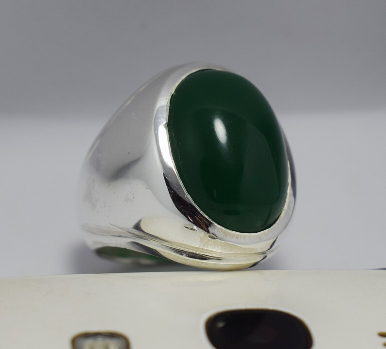 Pode incluir: Um anel de prata com uma grande gema verde oval.