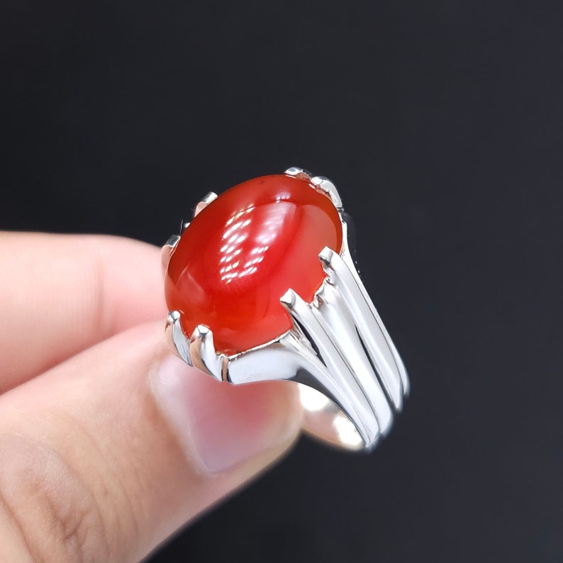 May include: A silver ring with a red gemstone. The ring has a detailed design with a raised setting for the stone.
