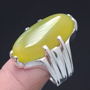 May include: A silver ring with a large, oval-shaped, yellow gemstone. The ring has a detailed, ornate design.