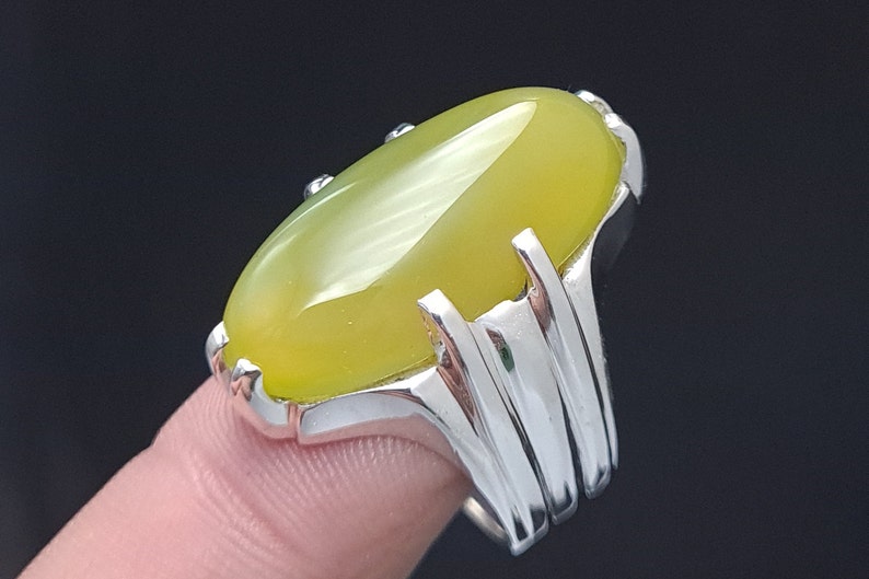 May include: A silver ring with a large, oval-shaped, yellow gemstone. The ring has a detailed, ornate design.