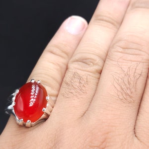 May include: A silver ring with a large, oval-shaped, red gemstone.