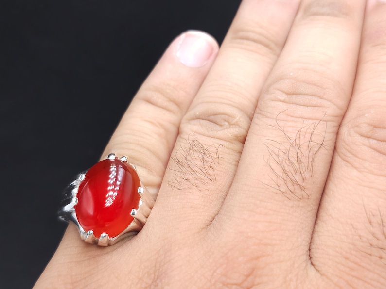 May include: A silver ring with a large, oval-shaped, red gemstone.