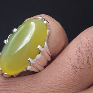 May include: A silver ring with a large, oval-shaped, yellow-green gemstone. The ring has a detailed, ornate design.