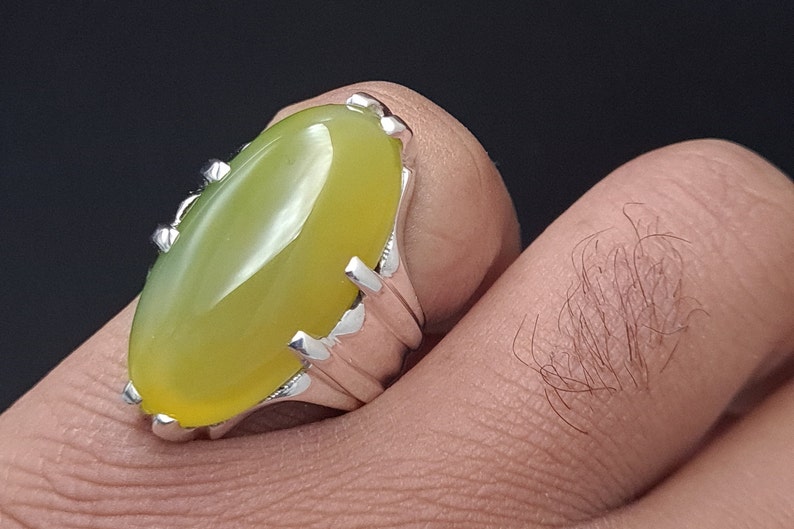 May include: A silver ring with a large, oval-shaped, yellow-green gemstone. The ring has a detailed, ornate design.