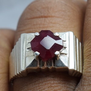 May include: A silver ring with a red gemstone set in a octagonal shape. The ring has a textured band.