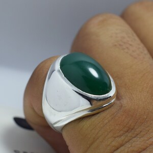 Pode incluir: Um anel de prata com uma grande gema verde oval.