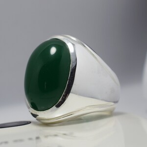 Pode incluir: Um anel de prata com uma grande gema verde oval.