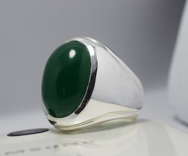 Pode incluir: Um anel de prata com uma grande gema verde oval.