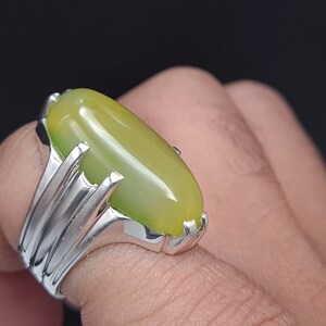 May include: A silver ring with a large, oval-shaped green gemstone. The ring has a detailed, ornate design.