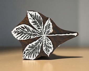 May include: A wooden printing block featuring a detailed leaf design. The leaf is white with black vein details, set against a dark brown background. The block is diamond-shaped with a handle, ideal for crafting and art projects.