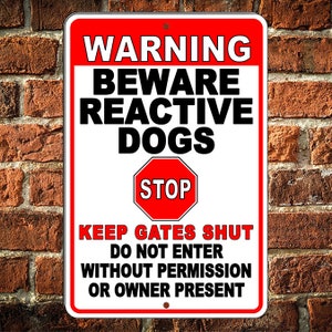 May include: A white metal sign with red lettering that reads "WARNING BEWARE REACTIVE DOGS STOP KEEP GATES SHUT DO NOT ENTER WITHOUT PERMISSION OR OWNER PRESENT". The sign has a red stop sign in the middle.