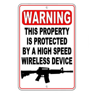 May include: A white sign with a red border and the text "WARNING THIS PROPERTY IS PROTECTED BY A HIGH SPEED WIRELESS DEVICE" in black. A black silhouette of a rifle is in the center of the sign.