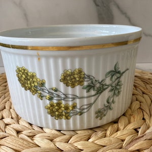 May include: White ceramic baking dish with a gold rim and a floral design featuring yellow flowers and green leaves.