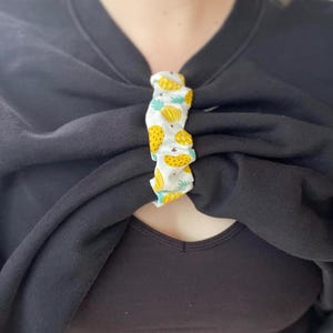 May include: A black sweatshirt with a pineapple-patterned fabric loop holding the neckline together.