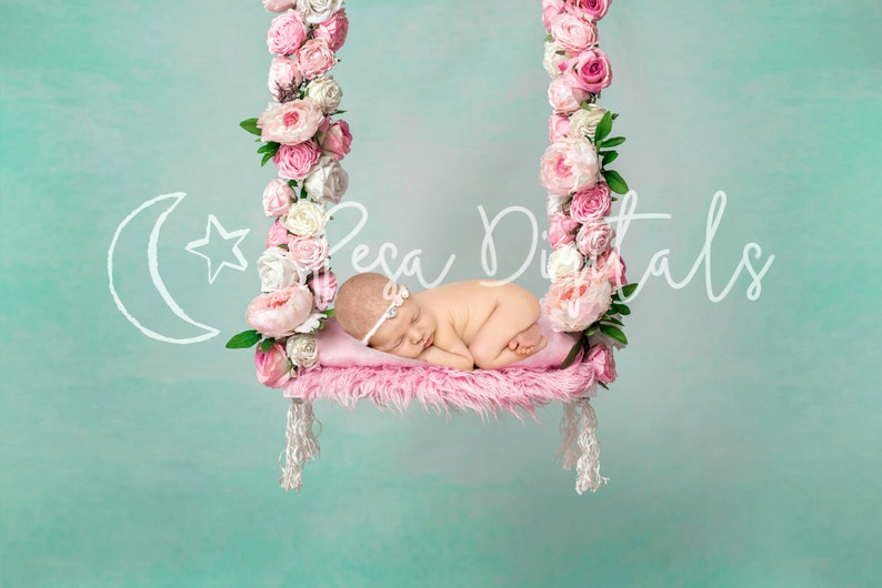 May include: A newborn baby sleeping on a pink swing decorated with pink and white flowers. The swing is hanging from a light blue background.