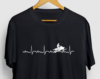 Puede incluir: Camiseta negra con un gráfico blanco de una moto de nieve con una persona conduciéndola, y una línea de latido del corazón encima.
